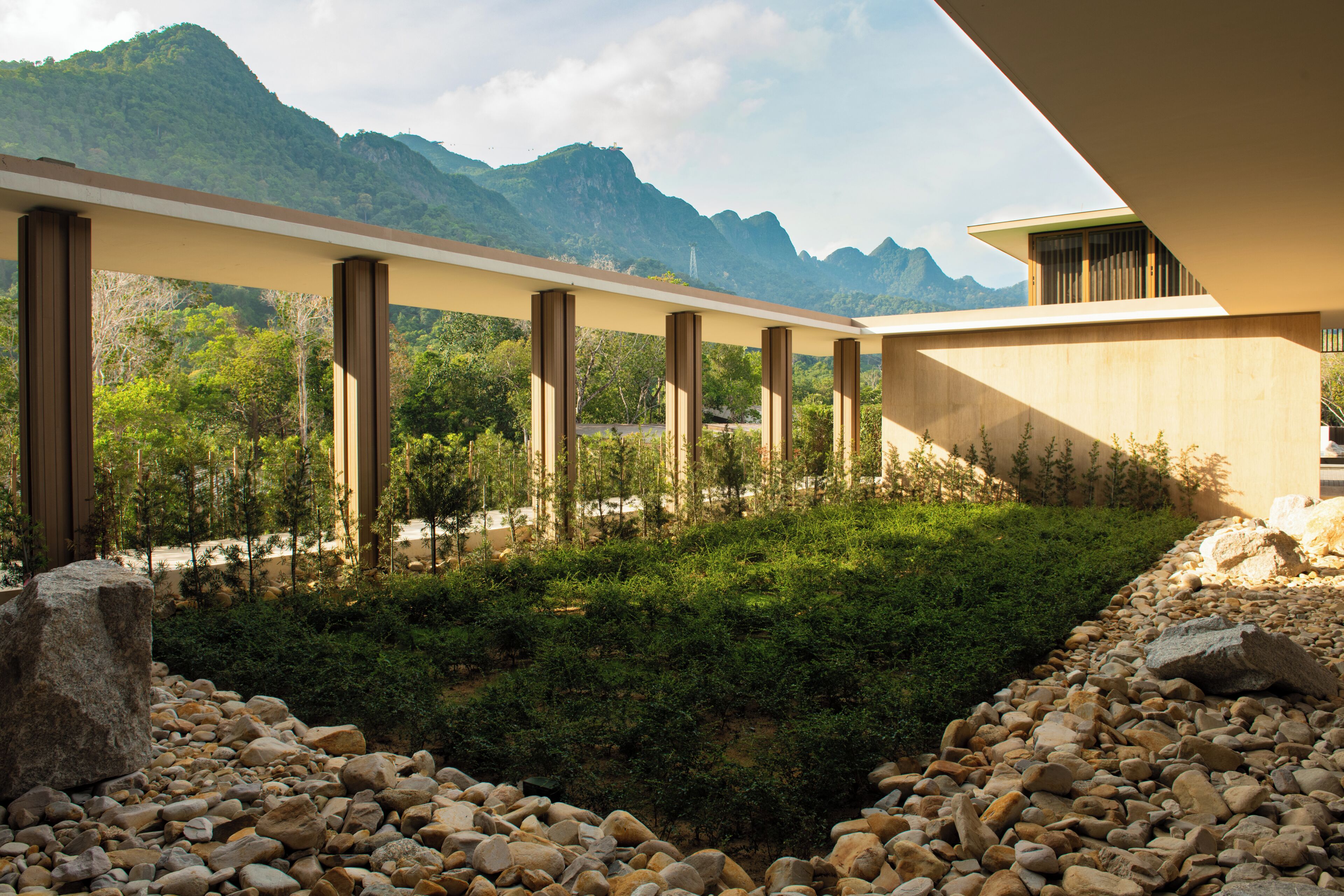 A modern building with a flat roof, a series of vertical columns, and a view of mountains in the background.