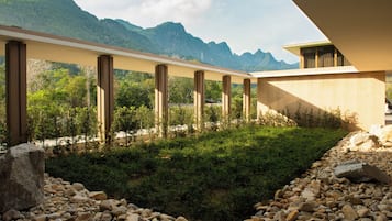 A modern building with a flat roof, a series of vertical columns, and a view of mountains in the background.