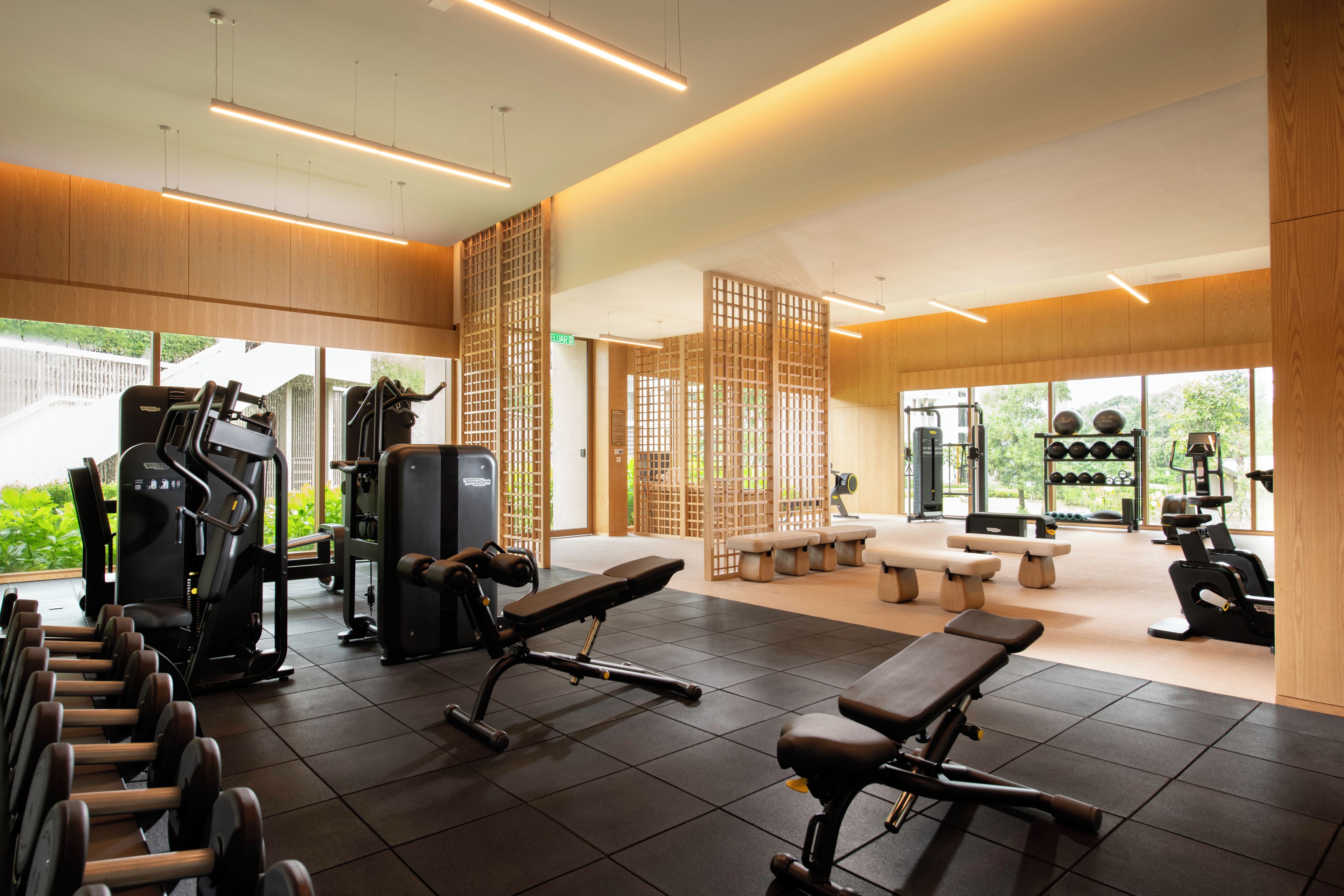 A gym with exercise equipment, benches, and a view of greenery outside.
