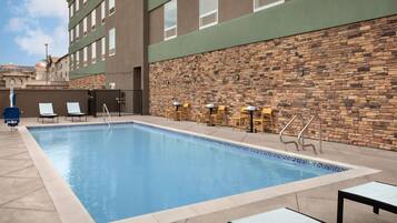 A rectangular swimming pool with a stone wall on one side and a building with multiple windows on the other.