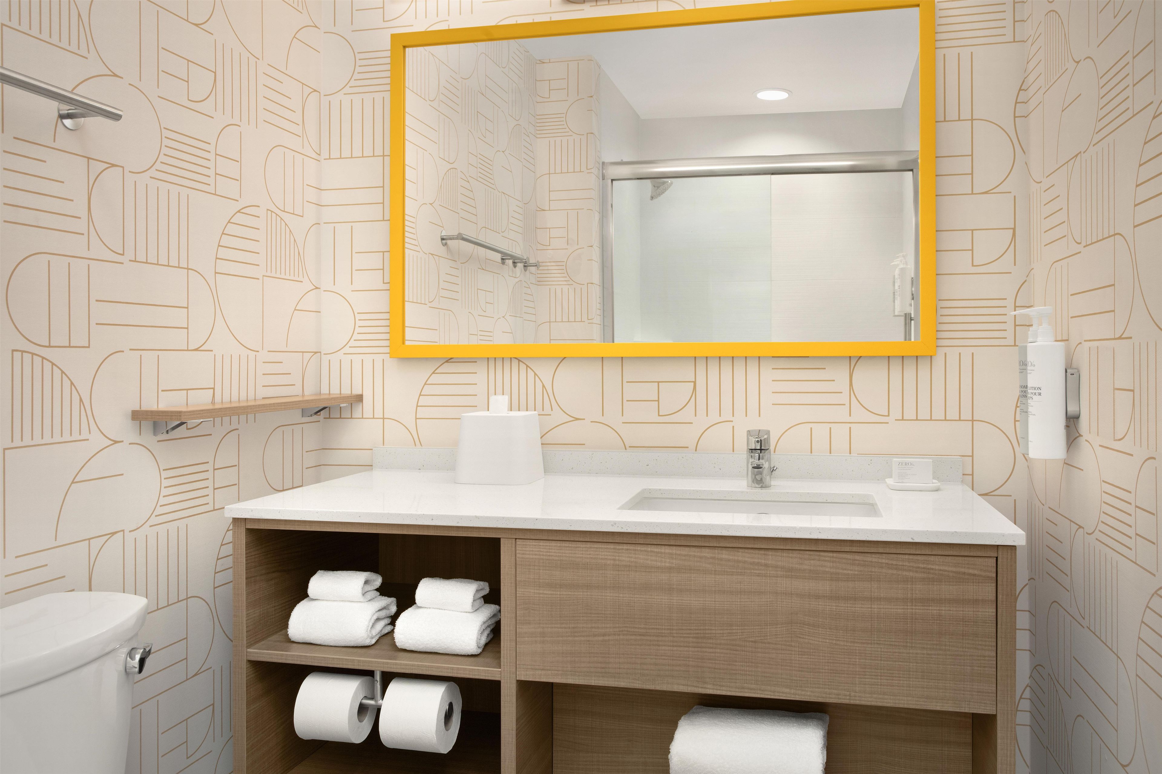 Un baño con un lavamanos blanco, un espejo con marco amarillo y papel tapiz estampado.