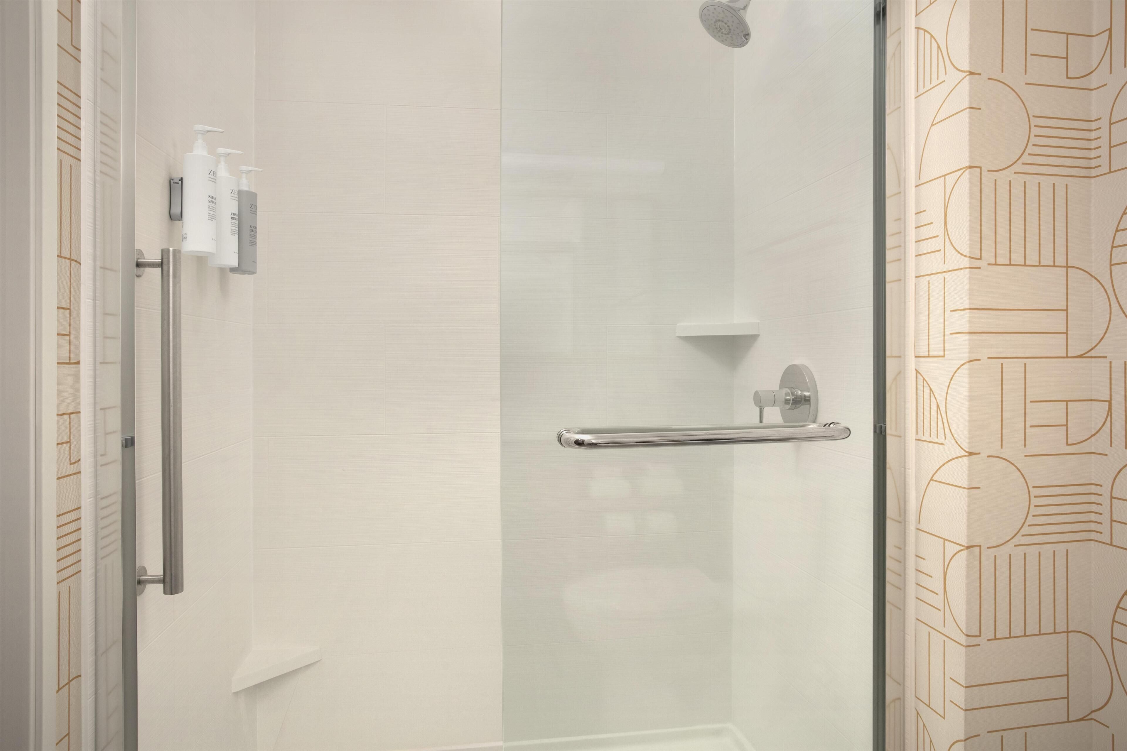 Une salle de bain moderne avec une douche à parois de verre, une barre d’appui et un porte-serviettes.