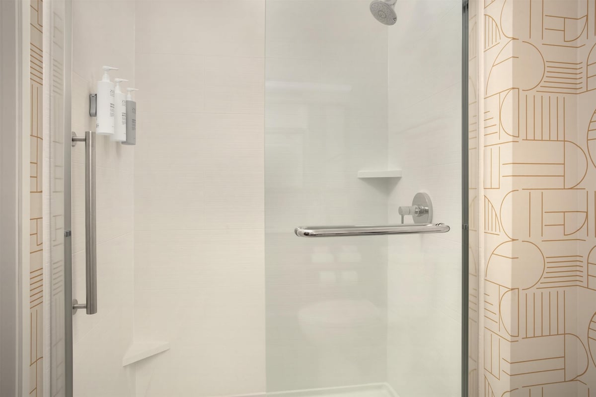 A modern bathroom with a glass shower enclosure, a handrail, and a towel rack.
