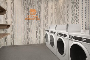 A laundry facility with multiple washing machines and a wall with a pattern of hanging teardrop shapes.