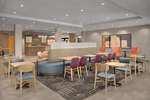 Een moderne hotelentree met zithoeken, een receptiebalie en een restaurant in de achtergrond.