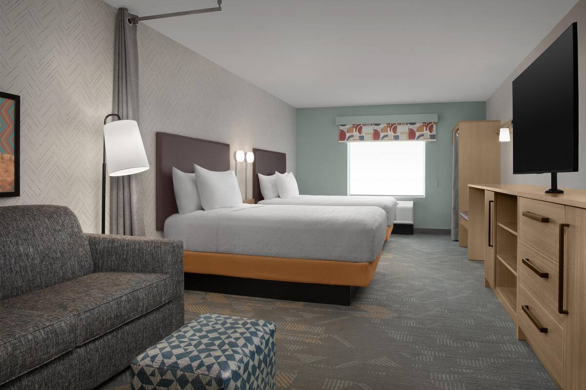 Une chambre d’hôtel avec deux lits, un canapé, une télévision et un bureau.