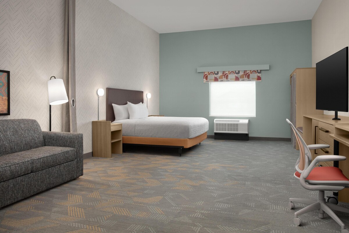 Habitación de hotel con cama, escritorio, silla, televisor, lámpara y ventana.