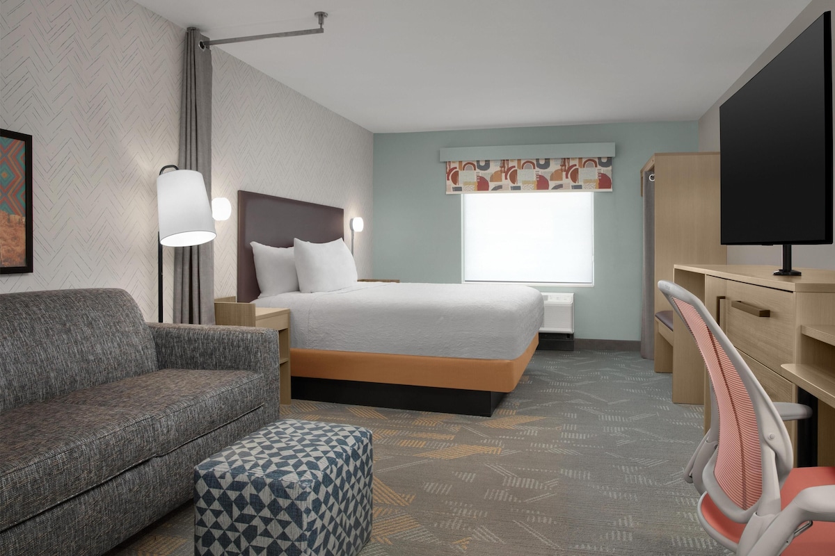 A hotel room with a bed, a sofa, a desk, a chair, a lamp, and a TV.
