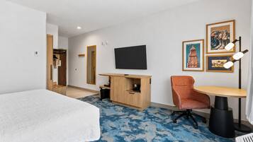 A hotel room with a bed, a desk, a chair, a television, and artwork on the wall.