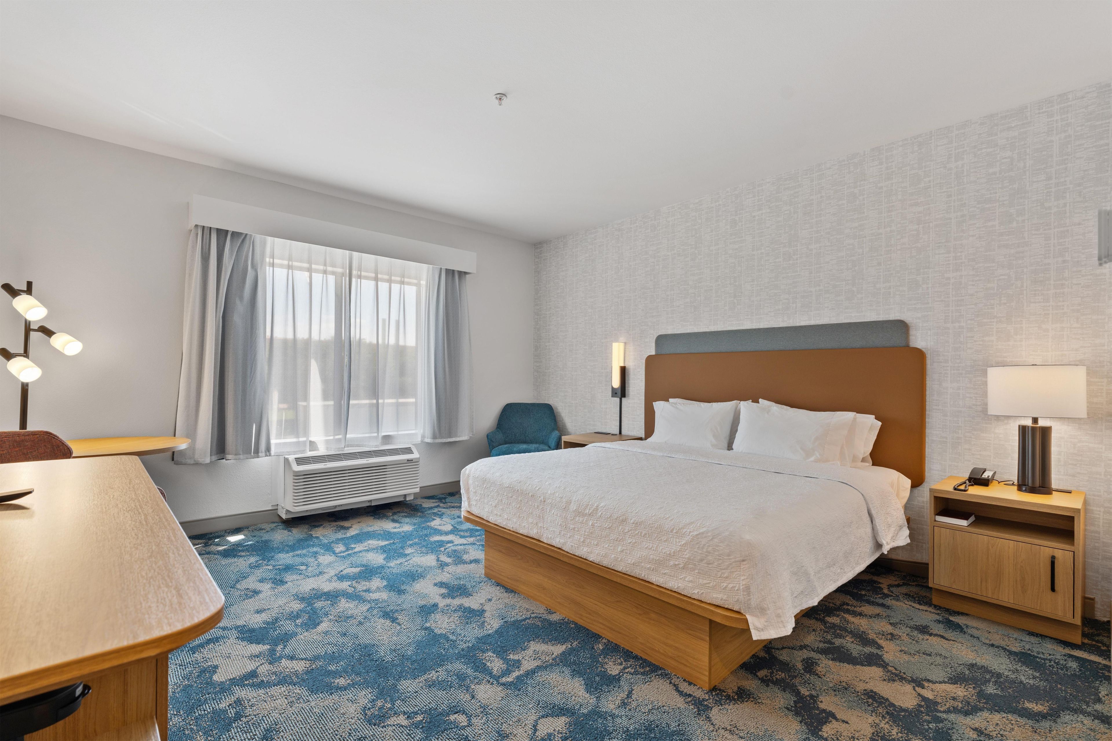 Une chambre d’hôtel comprenant un lit, une table de chevet, une lampe, une chaise et un bureau.