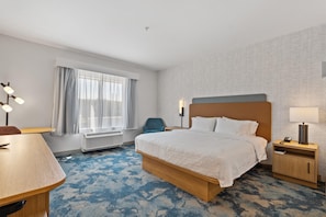 A hotel room with a bed, bedside table, lamp, chair, and a desk.