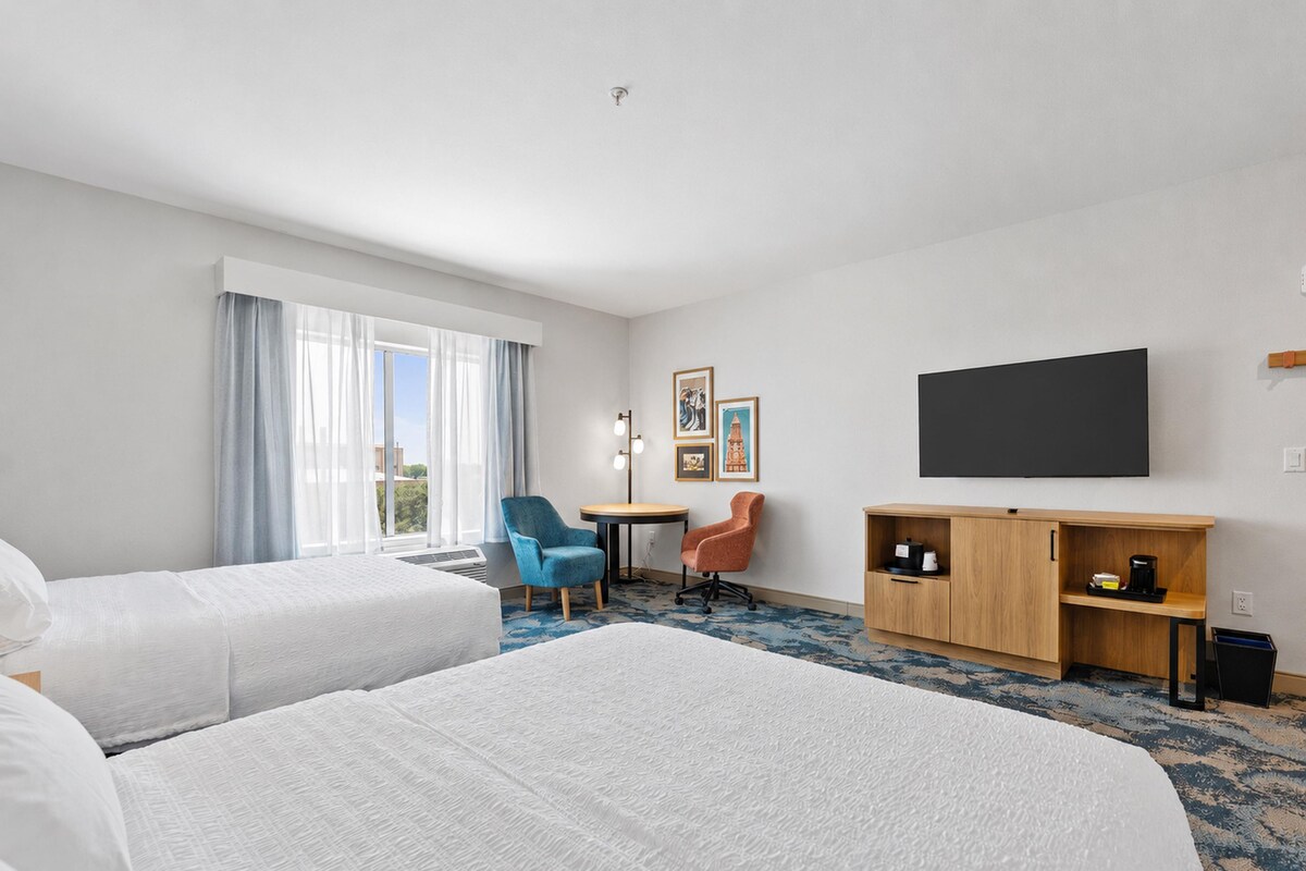 A hotel room with two beds, a desk, a chair, a TV, and a cabinet.