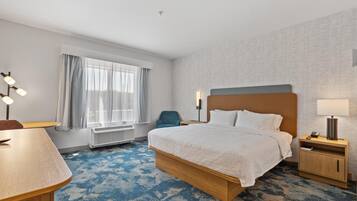 Una habitación de hotel con cama, mesita de noche, lámpara, silla y escritorio.