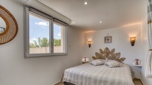 Een slaapkamer met een bed, een raam, een wandlamp en een decoratief object aan de muur.