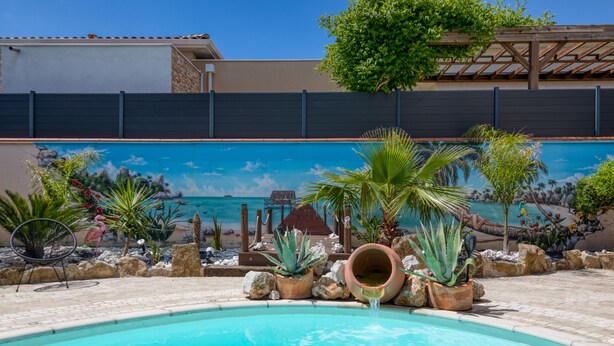 Zwembad met muurschildering, omringd door rotsen en planten, met een houten pergola erboven.