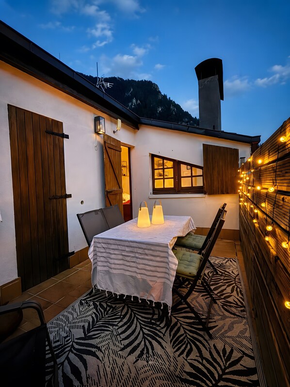 An outdoor patio with a table set for two, a wooden door, and a view of a mountain.