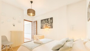 Ein Schlafzimmer mit einem Bett, Kissen, einem Nachttisch, einem Sessel, einem Heizkörper, einem Fenster und einer Tür.