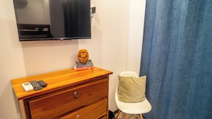 A wooden dresser with a television mounted above it, a plush toy on top, and a white chair with a cushion. - Beachfront Ocean-View Apartment in Gated Community (Parrita)