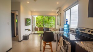 A modern kitchen with a large window, a water dispenser, and a dining area with chairs and a table. - Beachfront Ocean-View Apartment in Gated Community (Parrita)