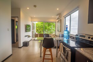 A modern kitchen with a large window, a water dispenser, and a dining area with chairs and a table. - Beachfront Ocean-View Apartment in Gated Community (Parrita)