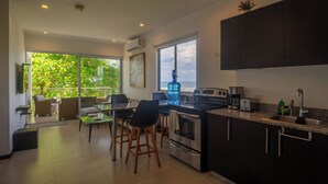 A modern kitchen with a large island, a dining area with chairs, and a view of the outdoors. - Beachfront Ocean-View Apartment in Gated Community (Parrita)