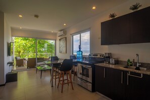 A modern kitchen with a large island, a dining area with chairs, and a view of the outdoors. - Beachfront Ocean-View Apartment in Gated Community (Parrita)