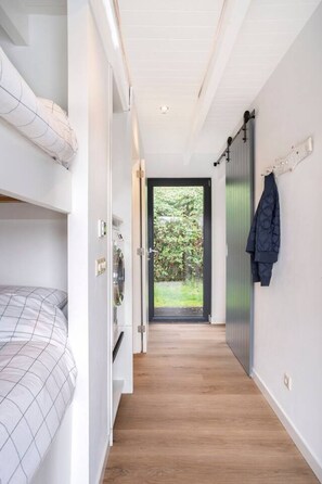 Un couloir étroit avec un lit superposé sur la gauche, une porte donnant sur l’extérieur et un porte-manteau sur la droite.