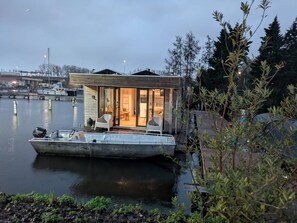 Une maison flottante avec un quai, un bateau et une vue sur l’eau et le paysage urbain.
