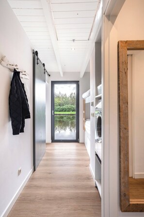 A hallway with a wooden floor, a coat rack, a door leading to a garden, and a washing machine.