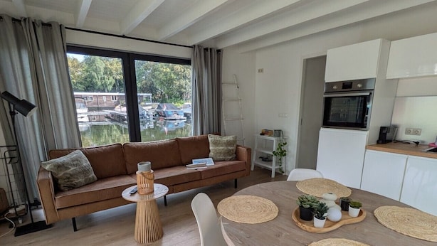 A modern living room with a sofa, a dining table with placemats, and a kitchen area with cabinets and appliances. - 6-persons Houseboat Experience in Amsterdam (Amsterdam)
