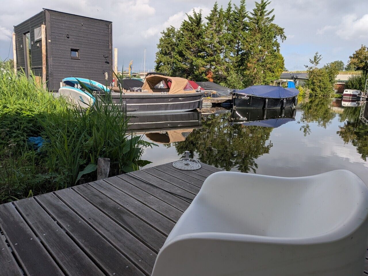 Une jetée en bois avec une chaise blanche, des bateaux et un petit bâtiment en arrière-plan.