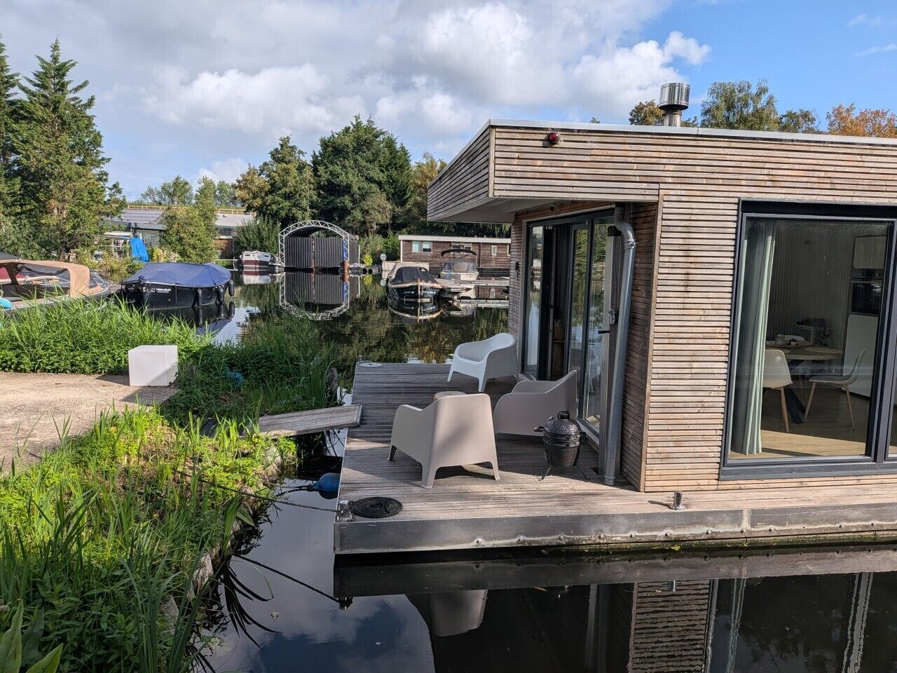 Een modern terras buiten, met een eethoek, met uitzicht op een waterpartij met boten.