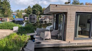 Een modern terras buiten, met een eethoek, met uitzicht op een waterpartij met boten.