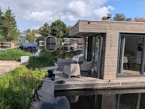 Een modern terras buiten, met een eethoek, met uitzicht op een waterpartij met boten.
