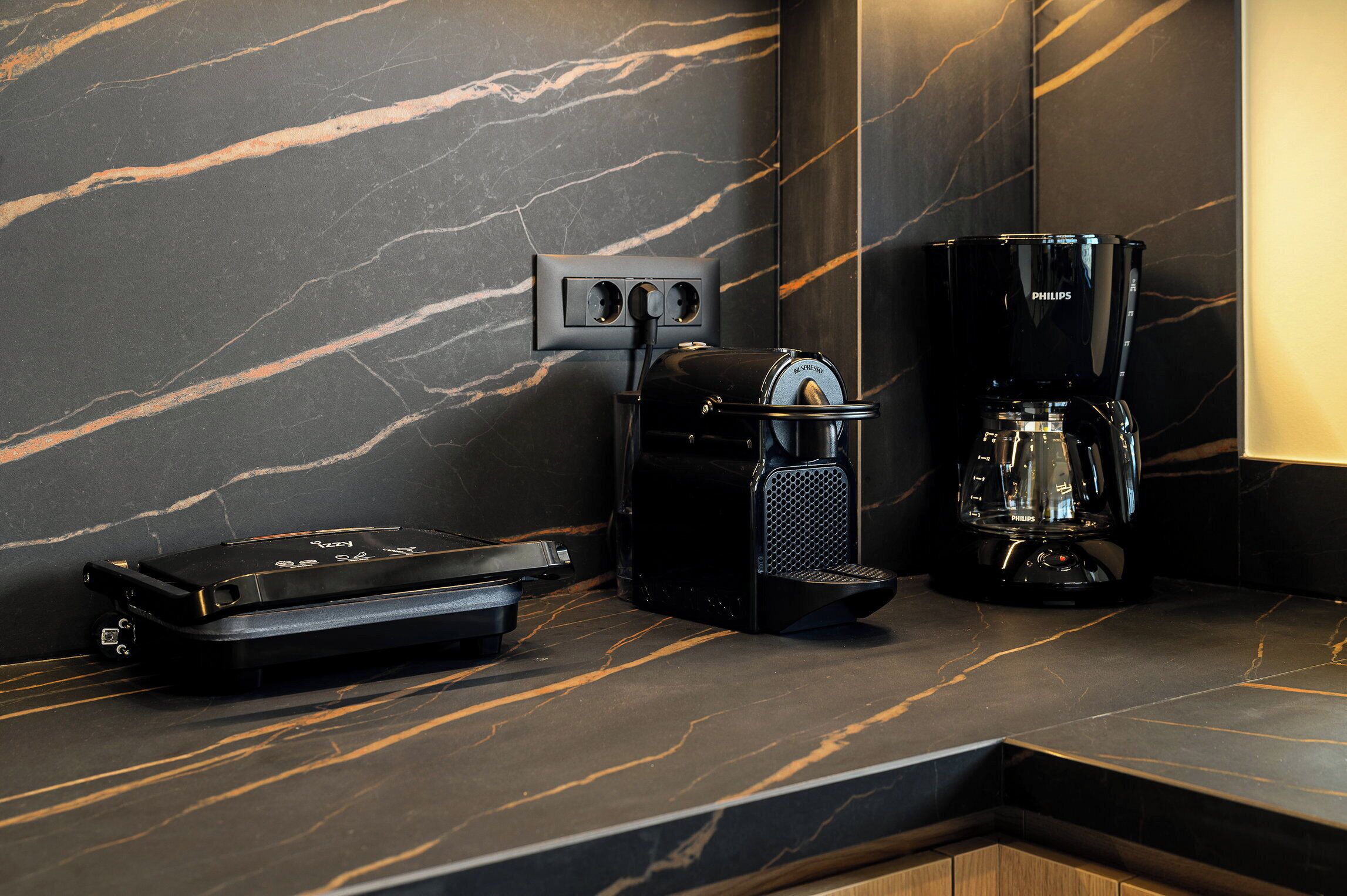 A modern kitchen with a marble countertop, a coffee maker, and a portable speaker.