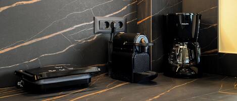 A modern kitchen with a marble countertop, a coffee maker, and a portable speaker.