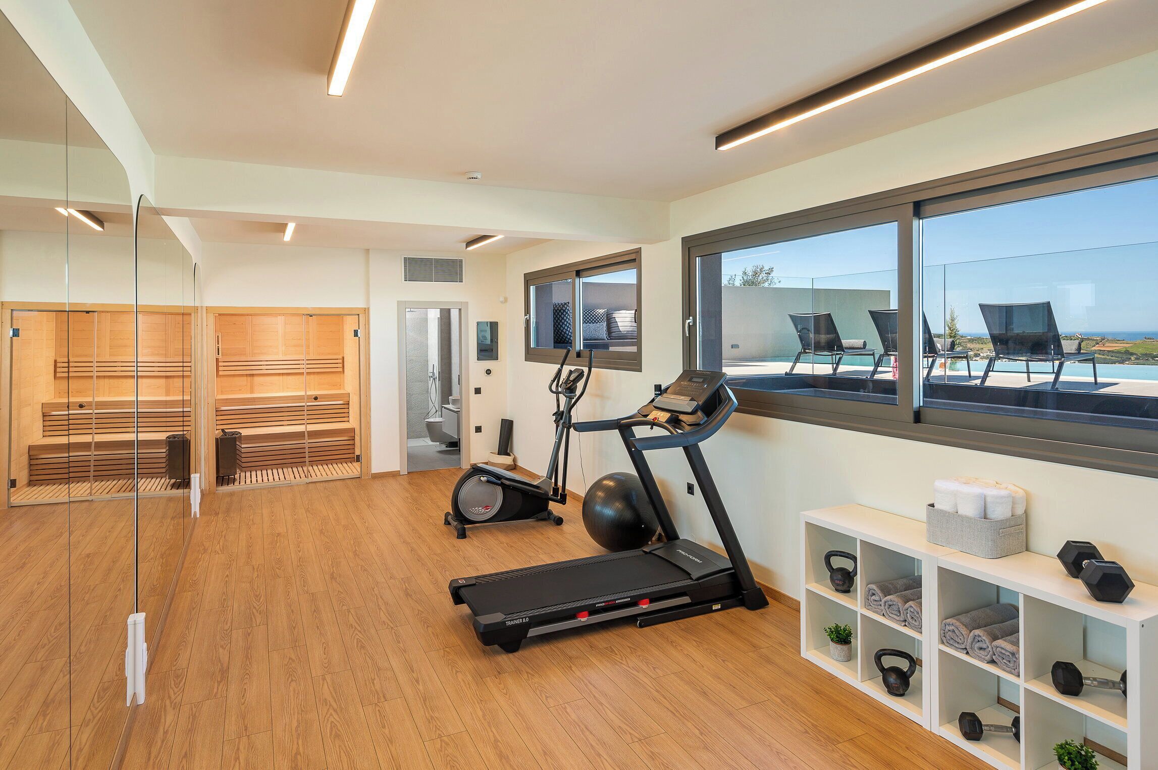 Une salle de sport moderne équipée de matériel d’exercice, dotée d’un plancher en bois et d’une grande fenêtre offrant une belle vue.