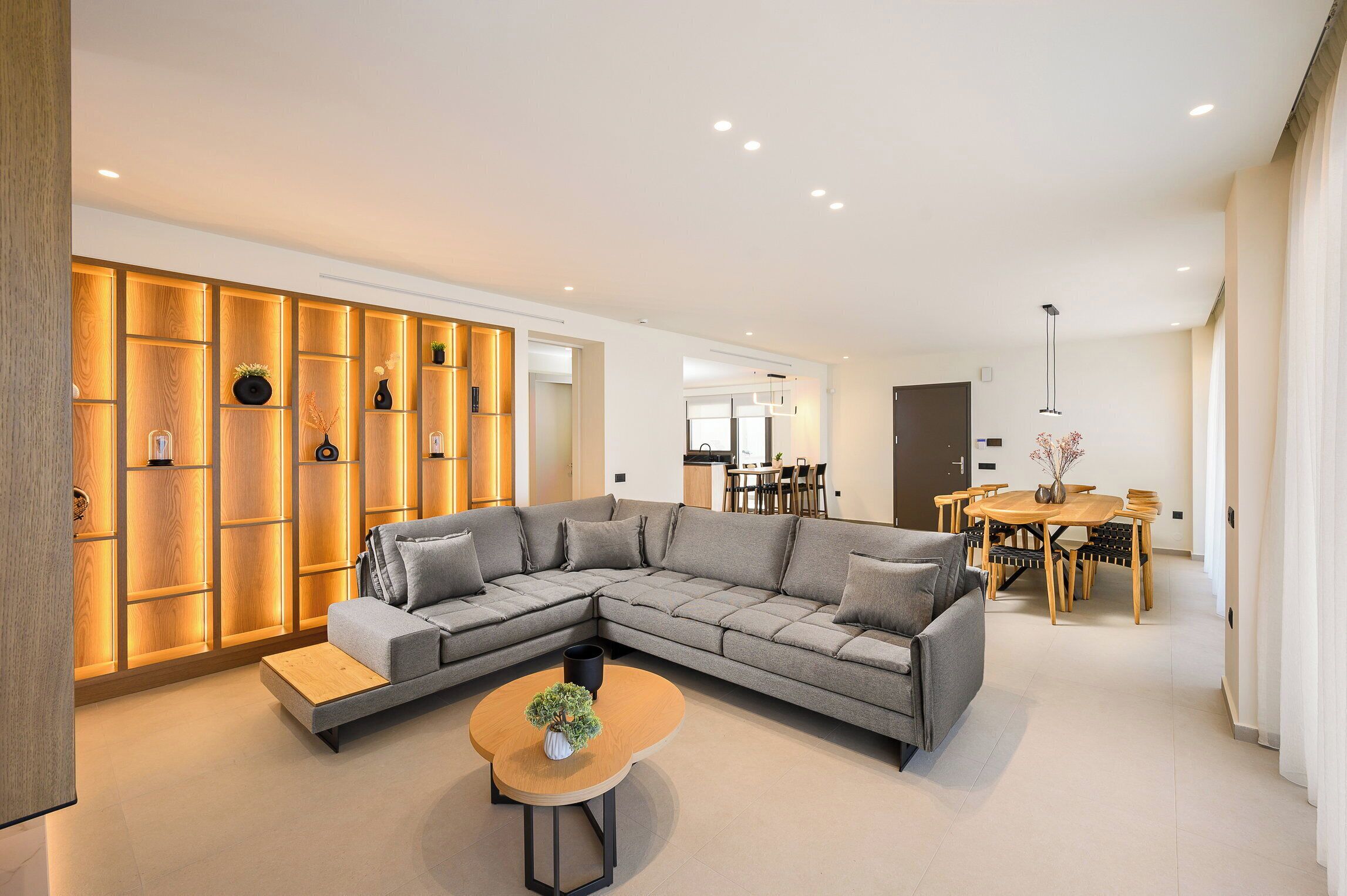 Un salon moderne avec un canapé d’angle, une table basse en bois et un coin repas comprenant une table et des chaises en bois.