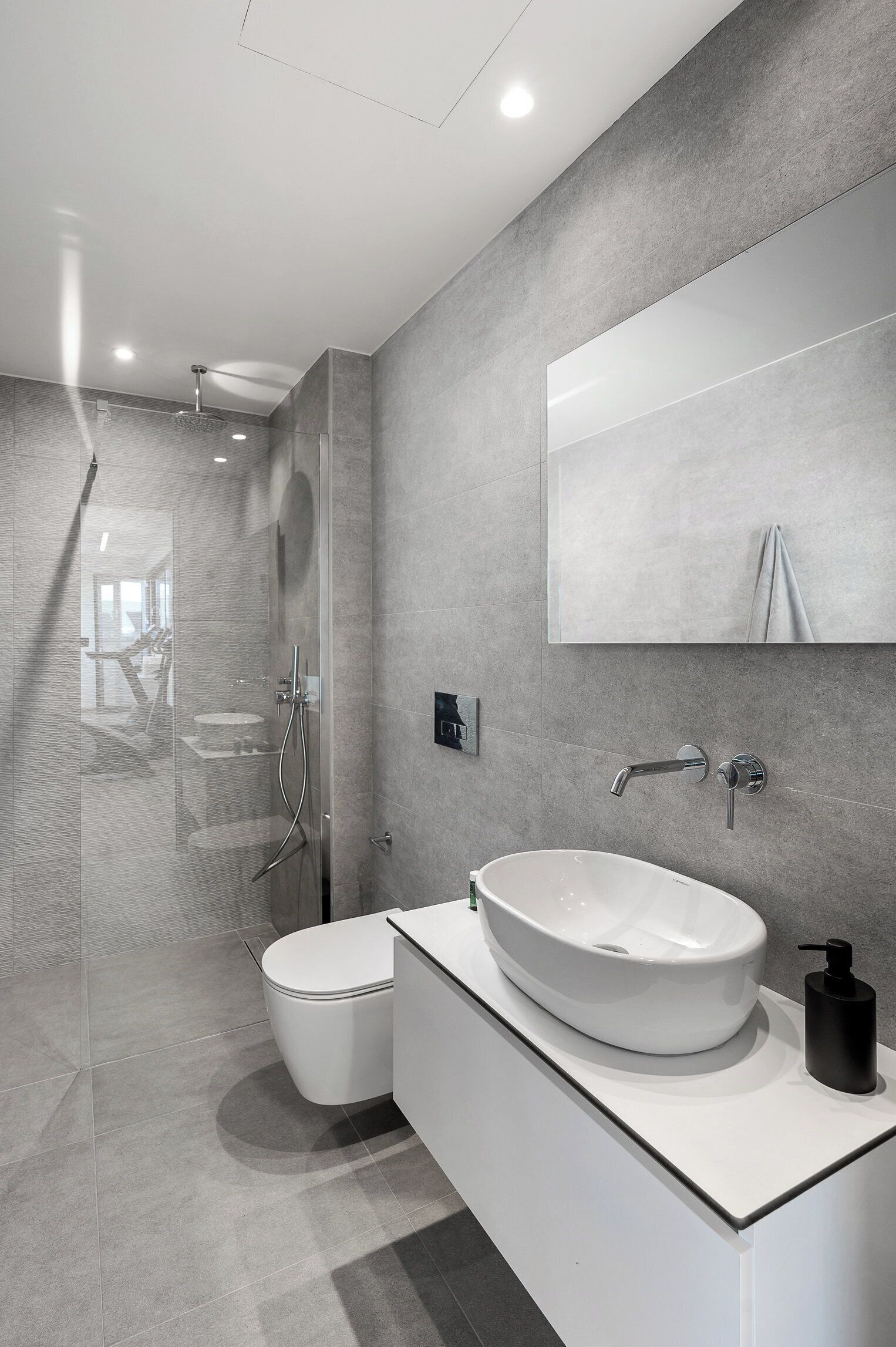 A modern bathroom with a glass-enclosed shower, a white sink with a vessel basin, and a large mirror above the vanity.