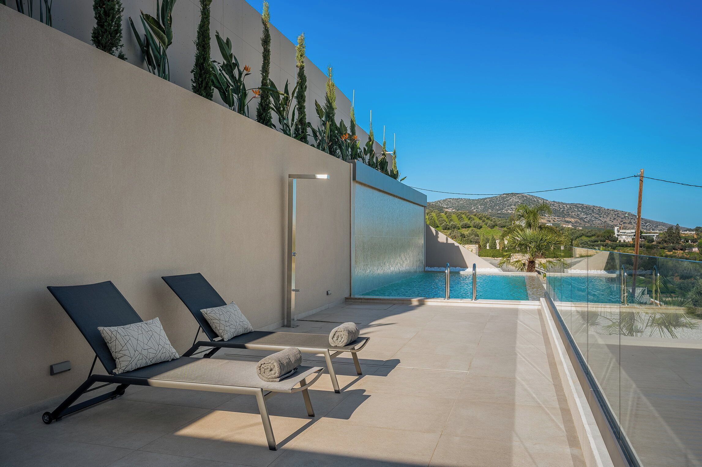 A modern outdoor pool area with lounge chairs and a clear view of a mountain and greenery in the background.