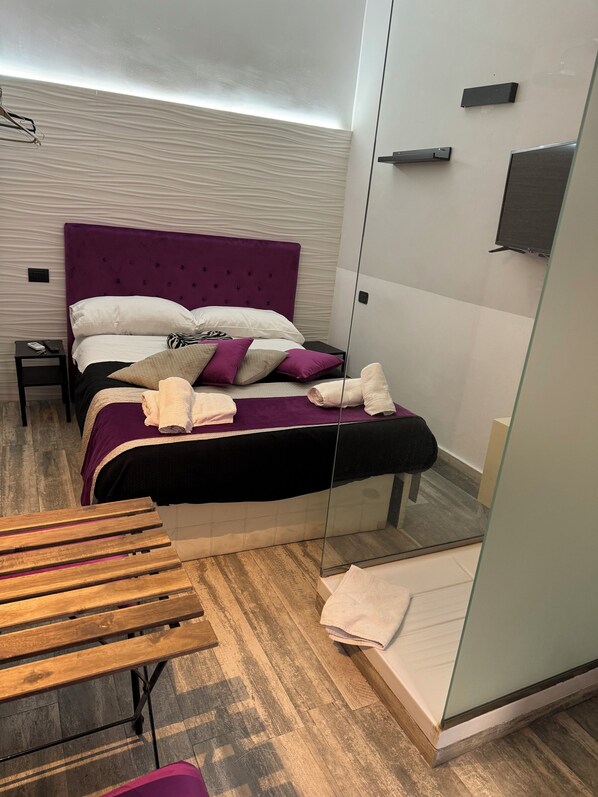 A modern bedroom with a purple headboard, a wooden bench, and a glass shower enclosure. - The Rooms at Volksplatz in Rome (Roma)