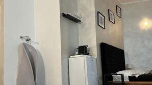 A modern room with a white toilet, a small white refrigerator, a bed with a dark headboard, and a wooden floor. - The rooms in the People's Square in Rome (Roma)