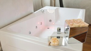 A modern bathroom with a large bathtub, a wooden side table with a rose, and a small decorative item on the table. - The rooms in the People's Square in Rome (Roma)