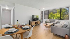 A modern living room with a dining area, grey sofa, wooden coffee table, and a TV on a wooden stand.