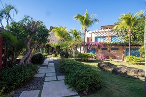 Trooppinen puutarha, jossa on polku, joka johtaa rakennukseen, jossa on olkikatto ja sininen ovi.