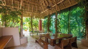 An indoor dining area with a large wooden table and benches, surrounded by lush greenery and a thatched roof. - Spacious luxury villa minutes from town, nearby beaches and attractions! (San Juan del Sur)