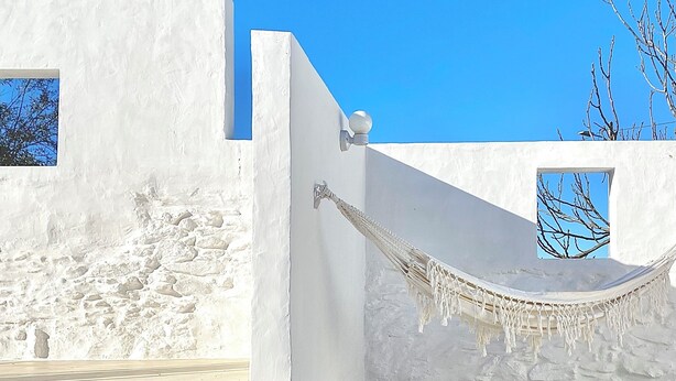 A white building with a stone wall, a hammock, and a clear blue sky. - Casa no Montinho  (Ourique)