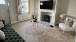 A modern living room with a green sofa, a round coffee table, a fireplace, and a flat-screen TV mounted on the wall.