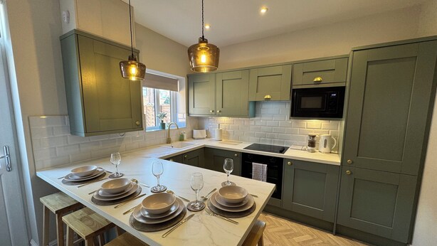 A modern kitchen with a central island, green cabinets, and pendant lighting.
