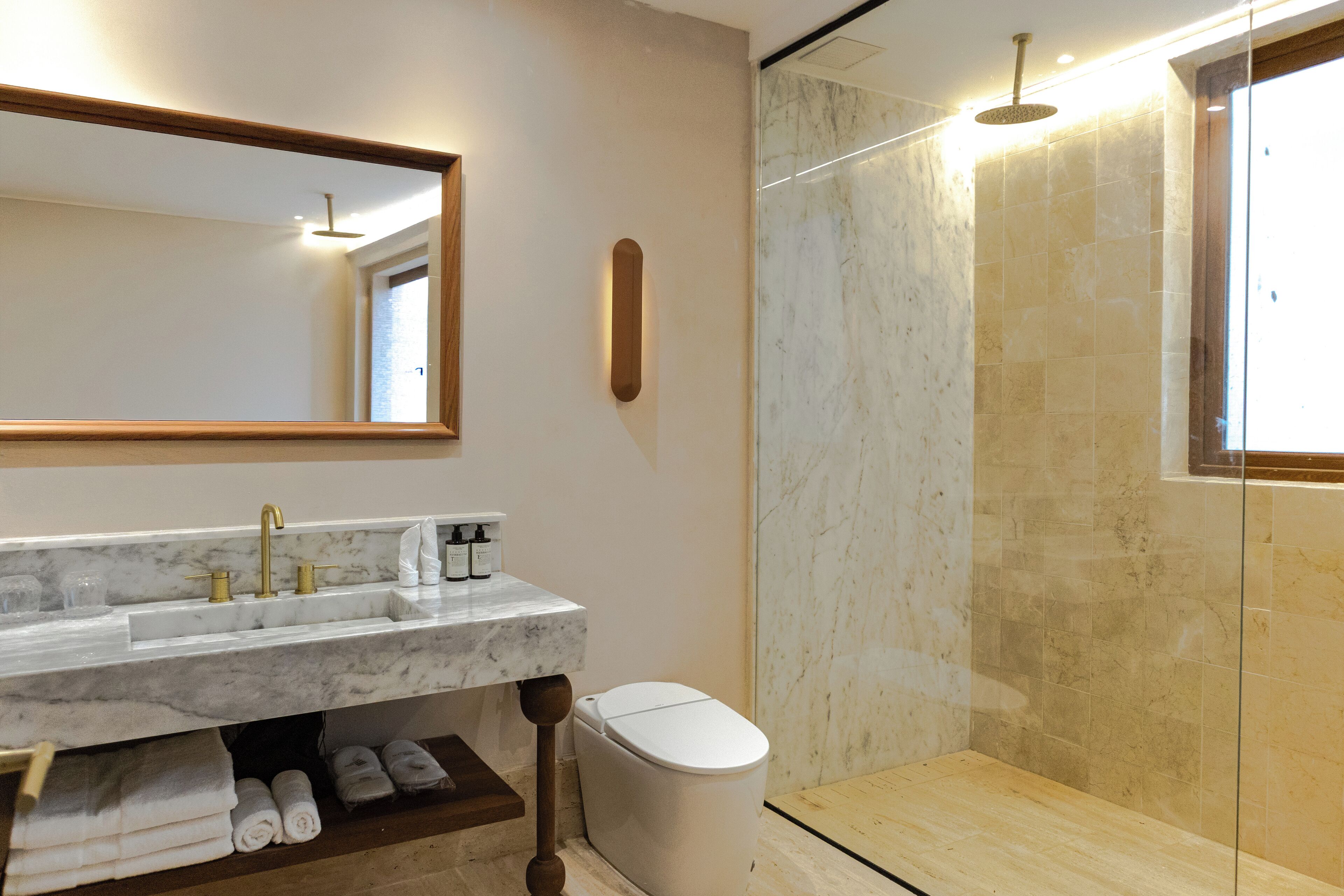 Un baño moderno con lavamanos de mármol, inodoro y cabina de ducha de vidrio.